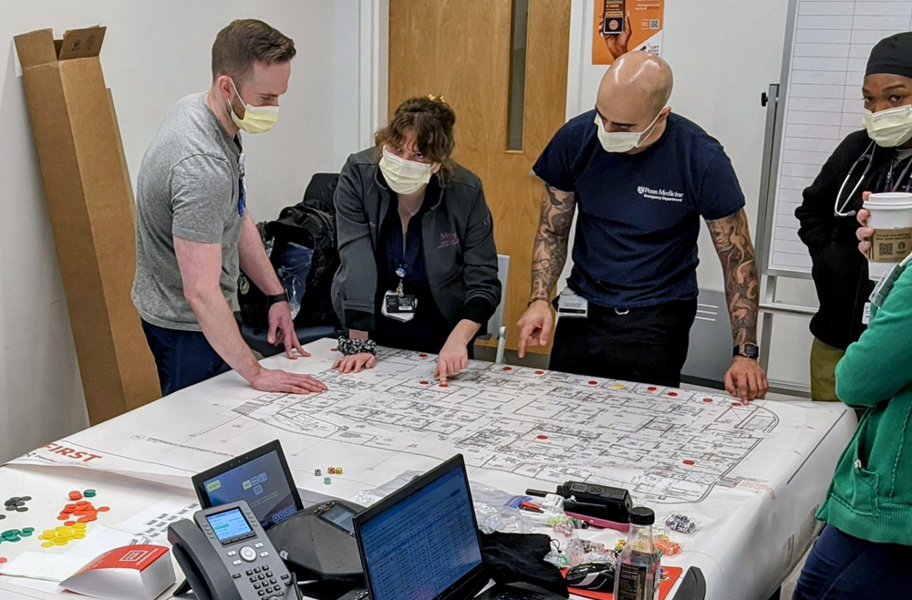 A group of Penn Medicine emergency responders with face masks look over plans during an emergency drill.