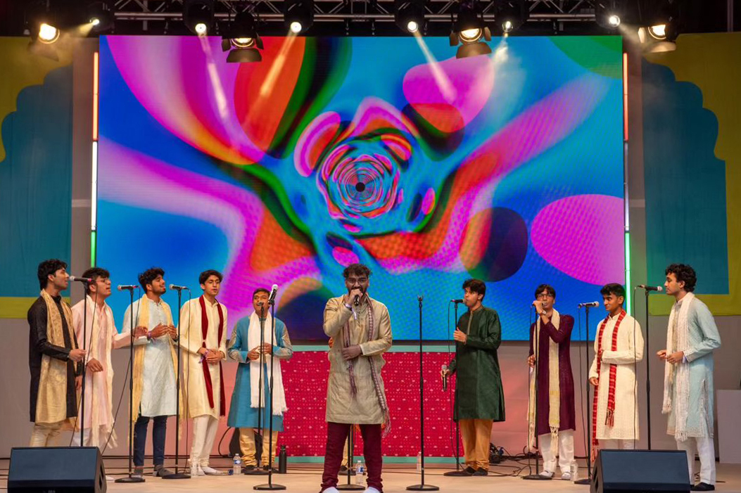 Ten people singing into microphones on a stage 