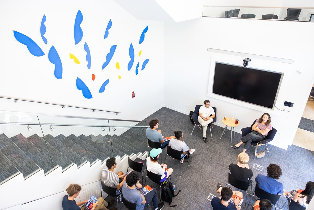 A stairwell and mural next to a group of students sitting in chairs.