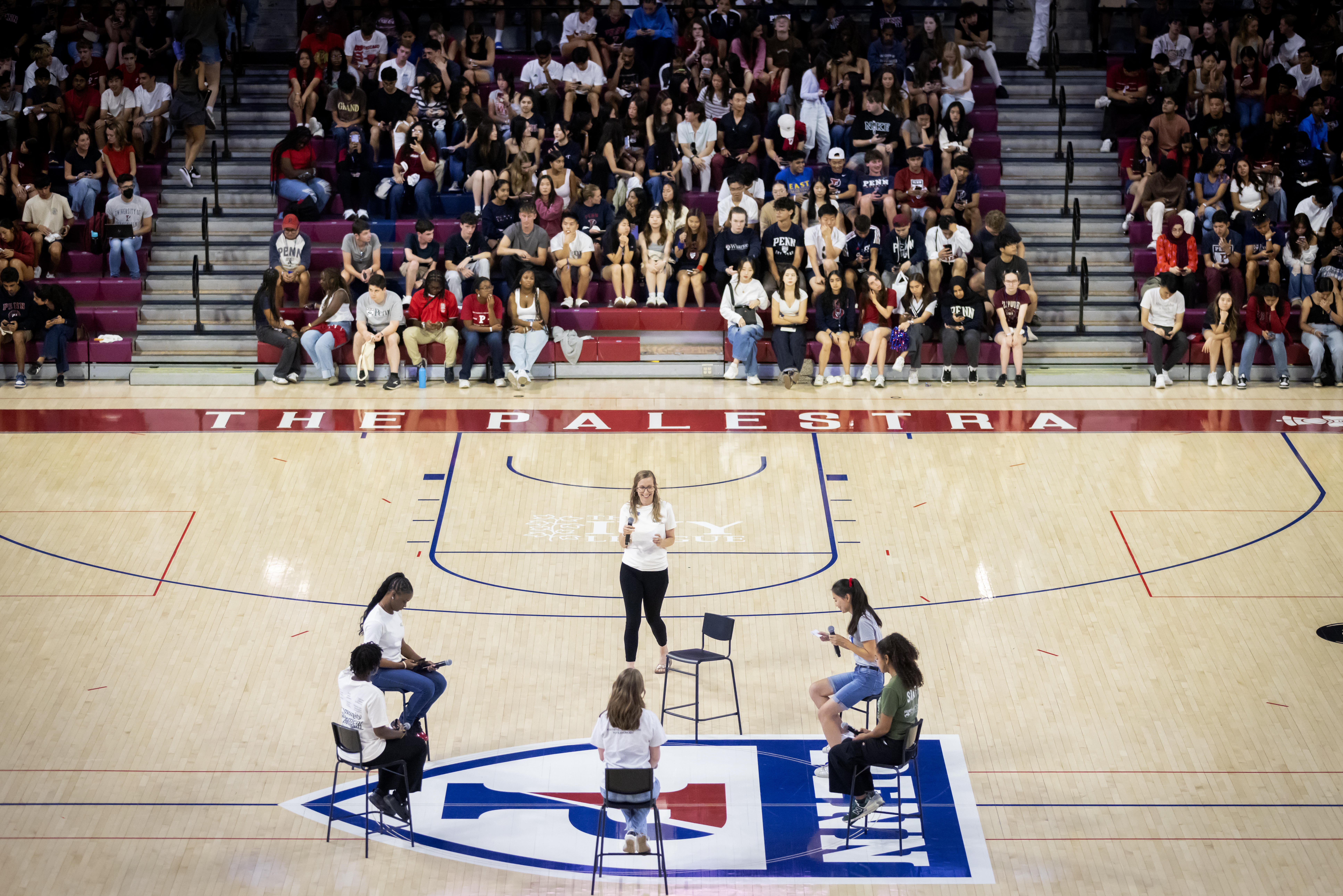 Speakers at the center of a gymnasium in roundtable-style chairs.