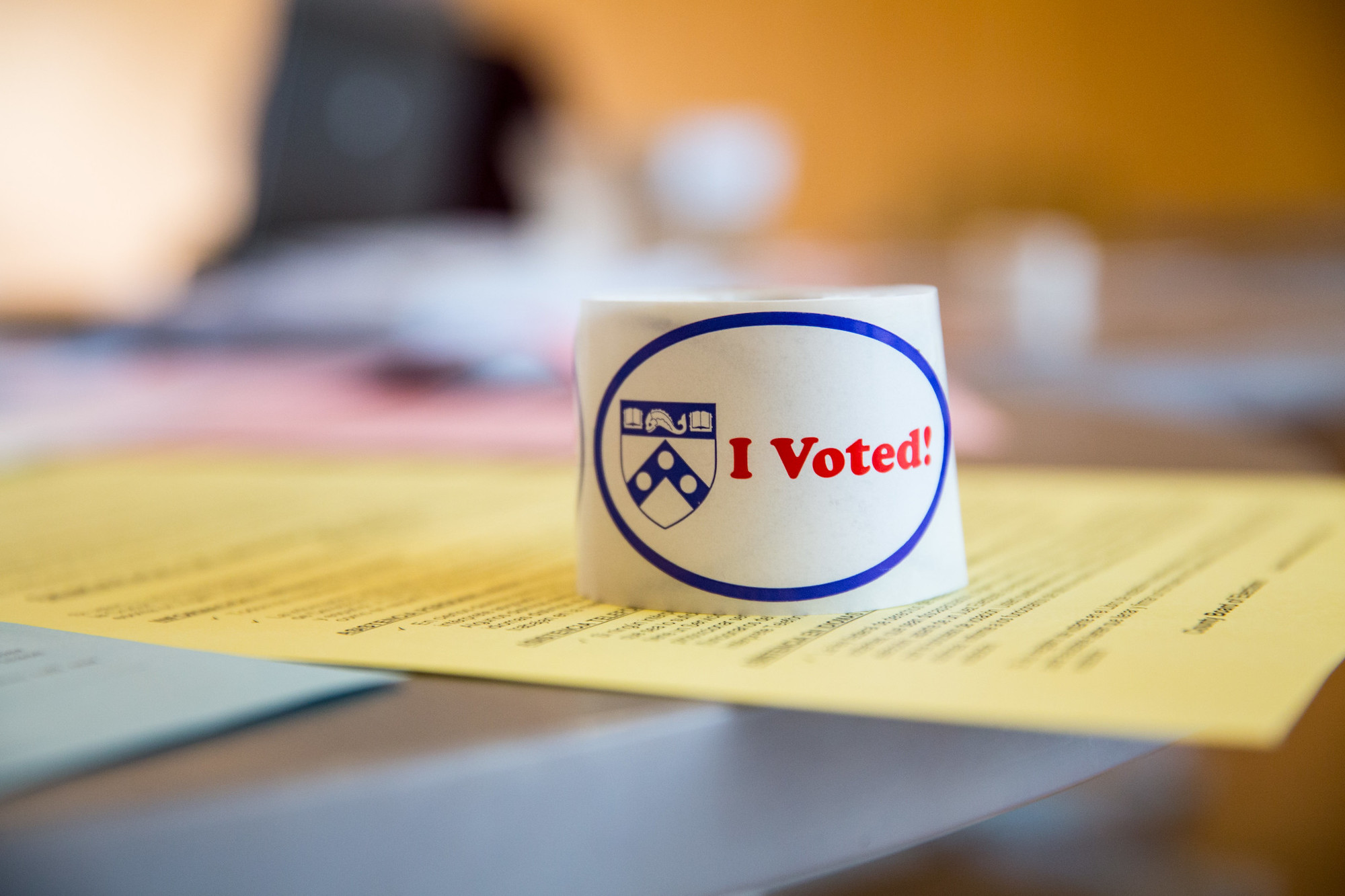 A roll of "I voted!" stickers with a Penn logo sits on top colored fliers on a table