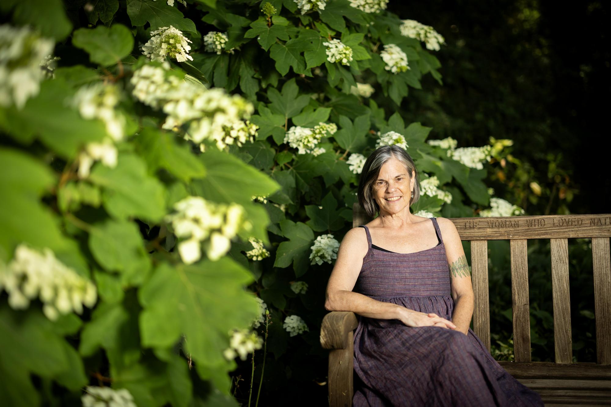 Jude Thachet sits on a wooden bench surrounded by hydrangeas