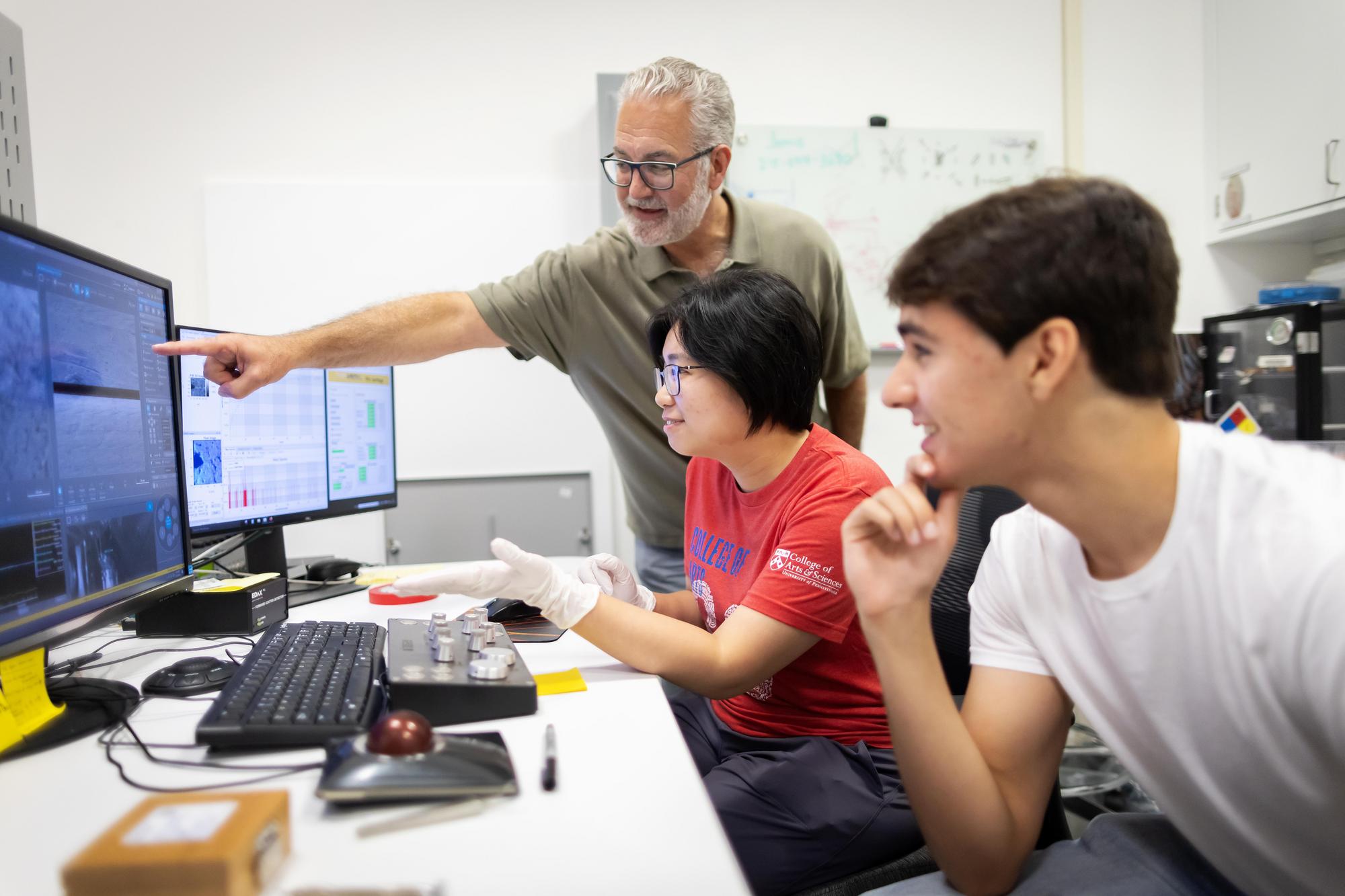 A.T. Charlie Johnson, Yue Jiang, and Vincent Kerler work in a lab staring at a computer scrreen.