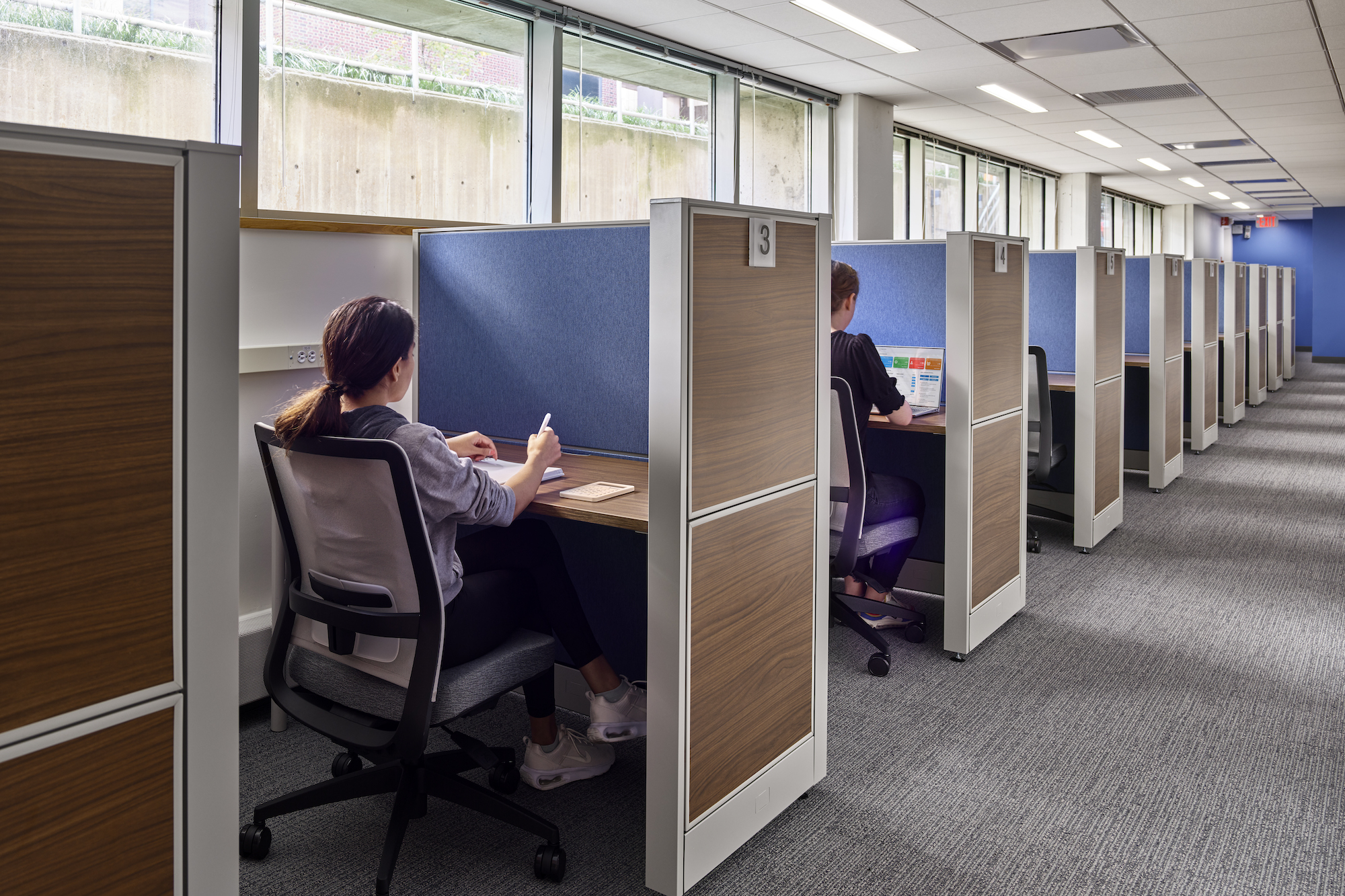 Along a long room, individual cubicles are set up for students taking tests privately. 