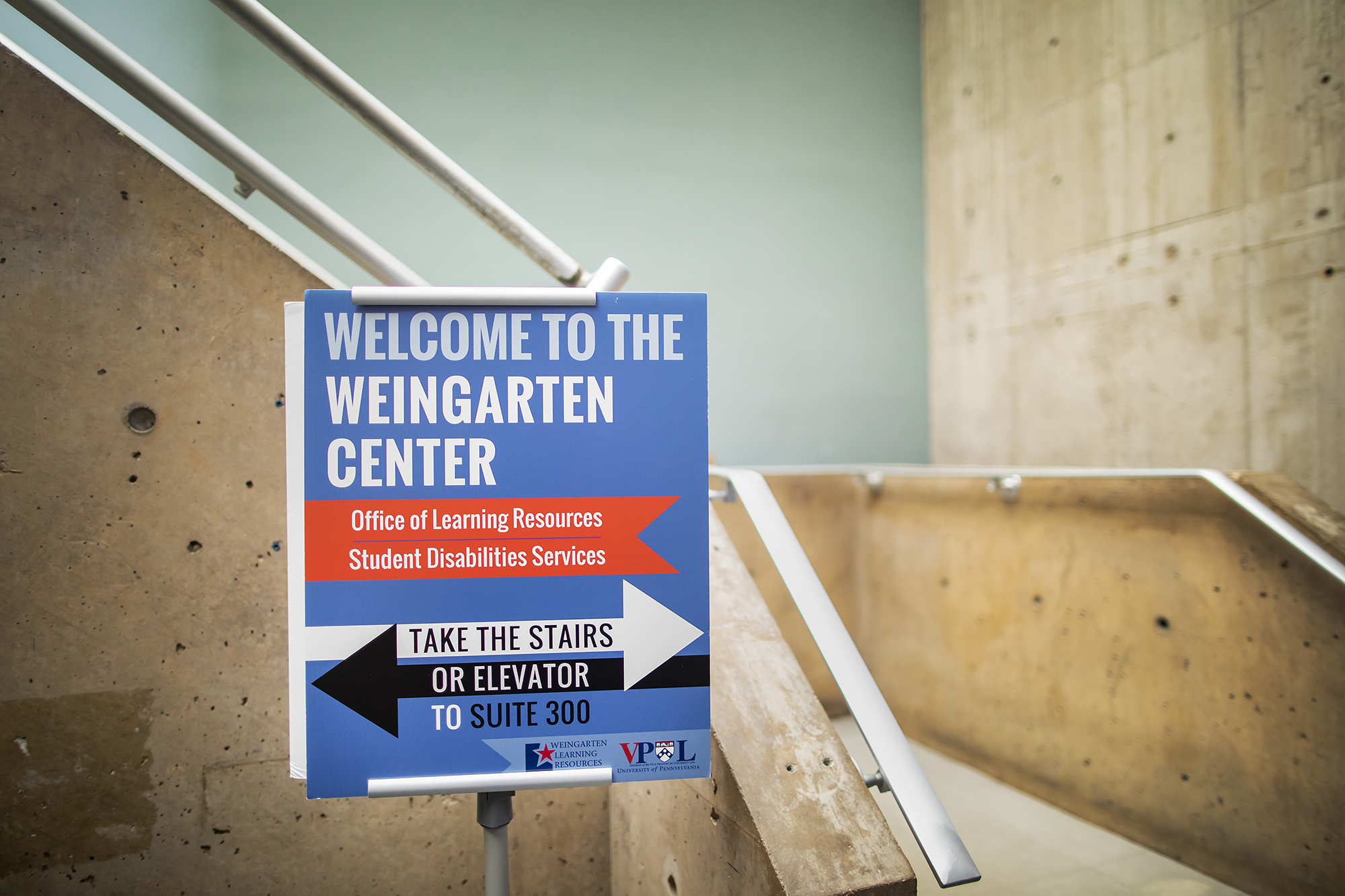 A sign in front of a stairwell reading, "Welcome to the Weingarten Center, Office of Learning Resources, Student Disabilities Services. Take the stairs or elevator to suite 300