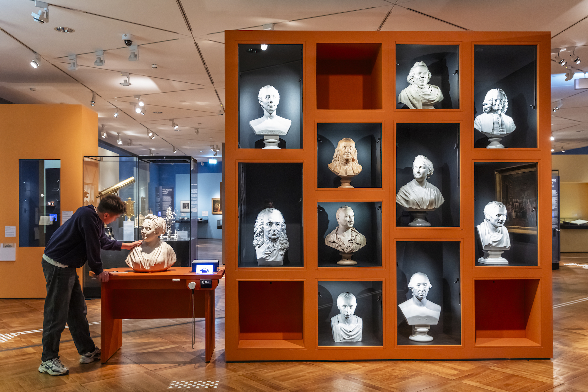 A man looks at a stand-alone wall of carved busts in niches