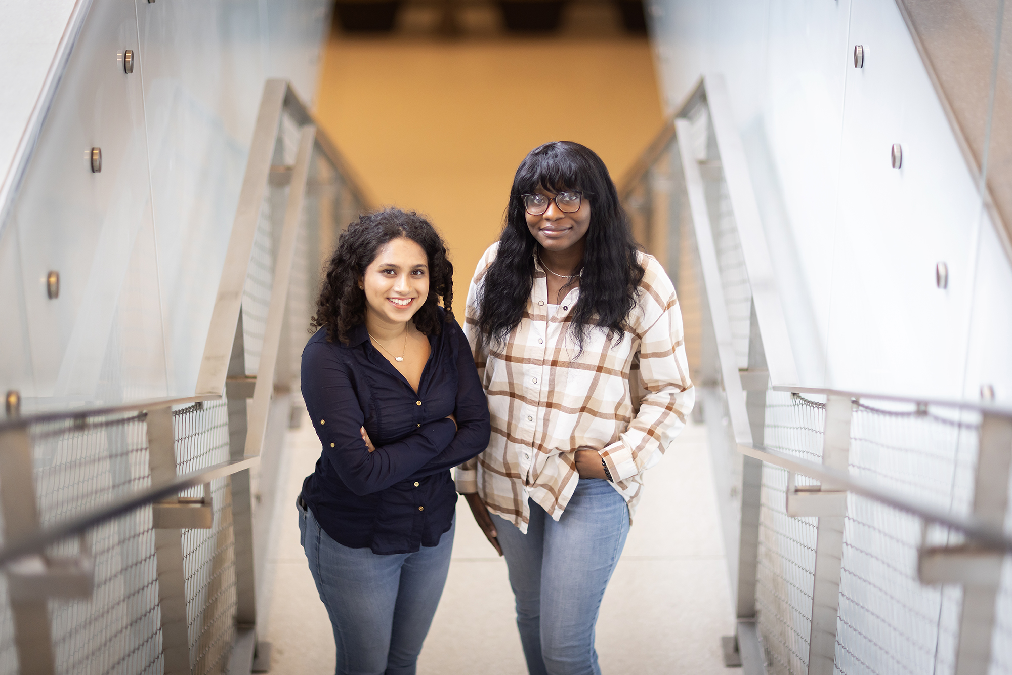 Ziana Sundrani and Taiwo Adeaga pose next to each other with their arms folded.