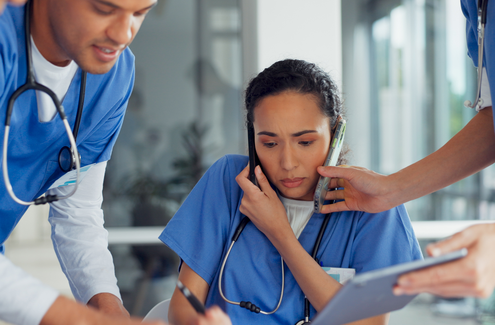 Three nurses with smartphones and charts looking overworked.