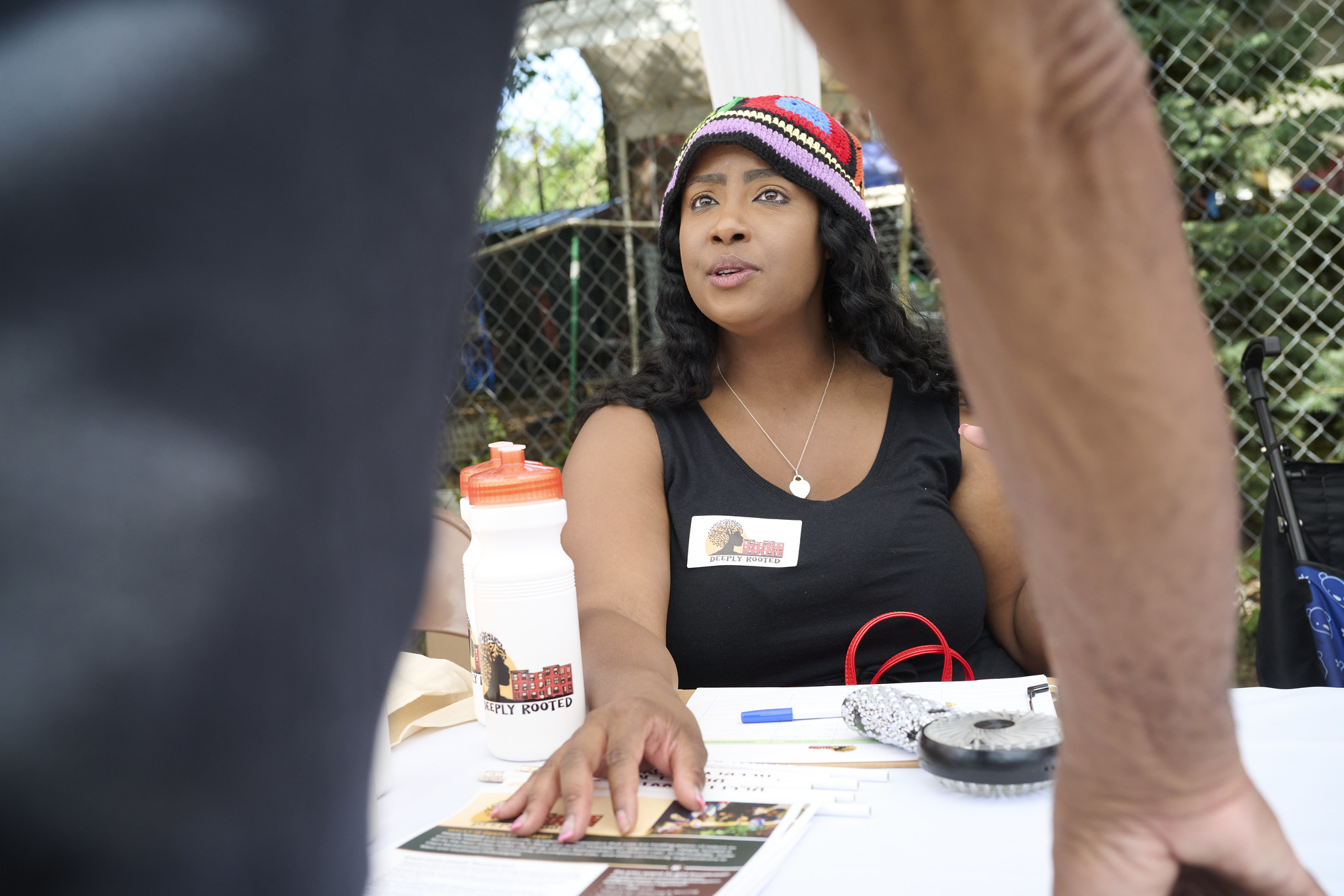 Janaiya Reason, wearing a Deeply Rooted name badge, talks with a person at a table at an outdoor community event.