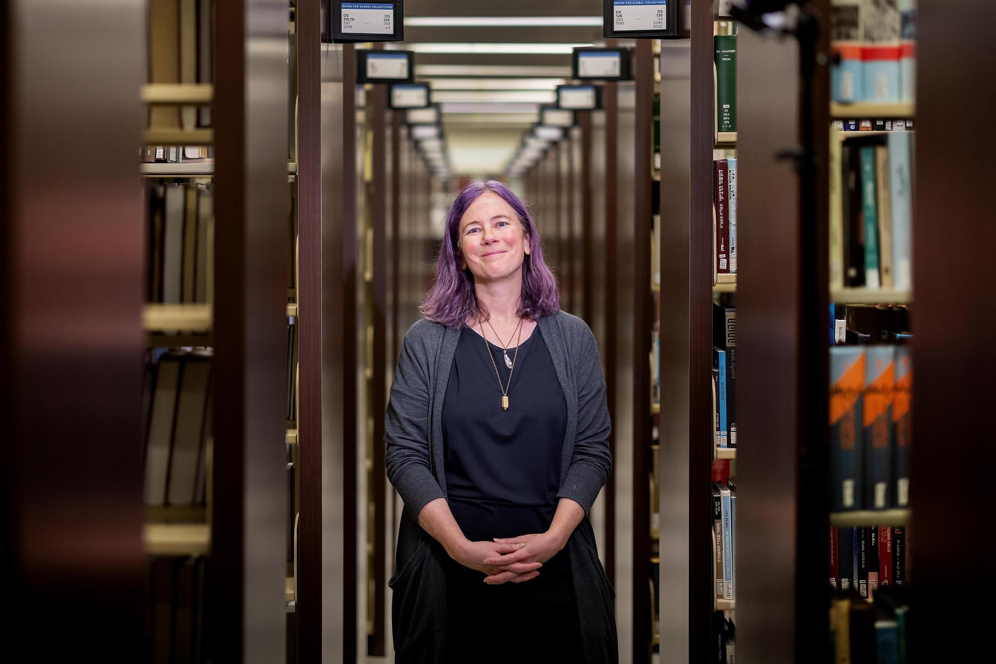 Brie Gettleson stands in the library stacks, hands folded.