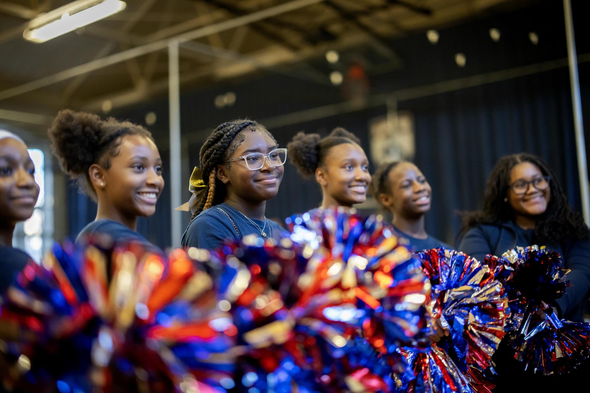 A row of older West Philadelphia students smiles and poses with their pompoms