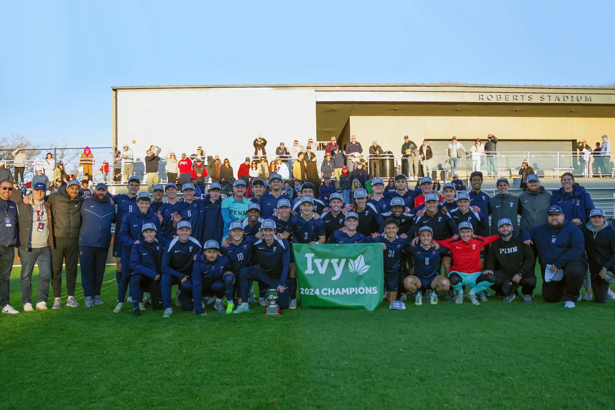 Penn’s men’s soccer team pose for a photo on the field while holding banner that ready Ivy 2024 champions.