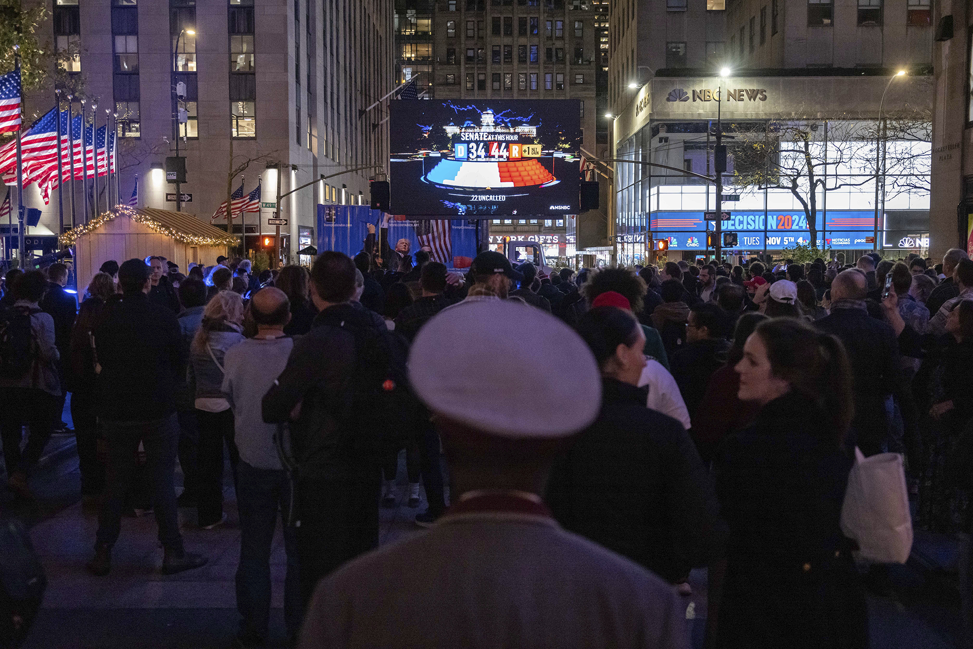 A group of people, seen from behind, watch election results from NBC News on a livestream display at Rockefeller Center in New York City.