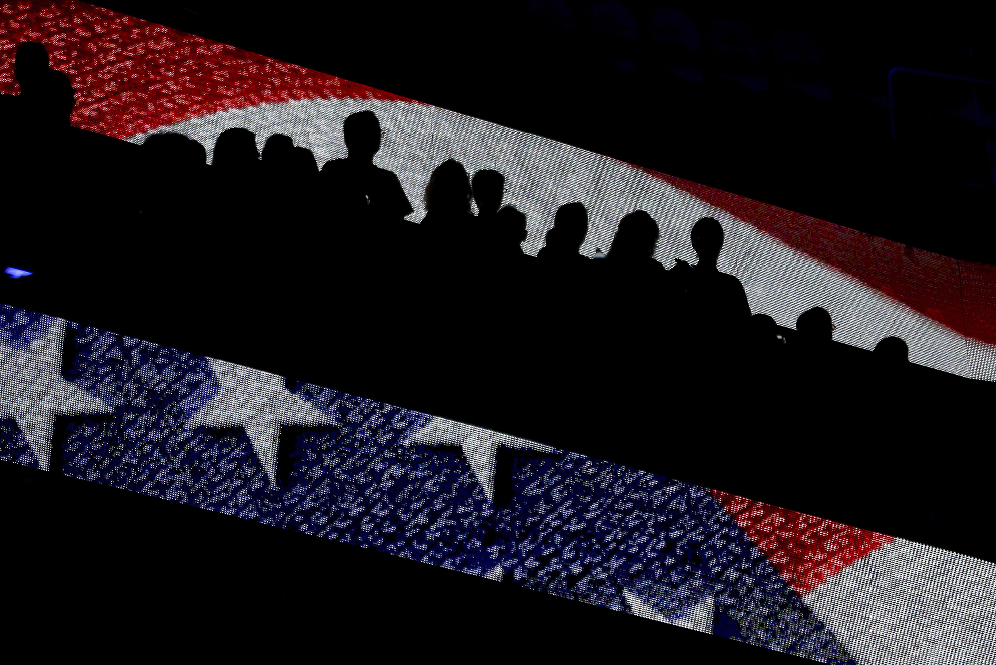 People in bleachers covered by an illuminated portion of the American flag.