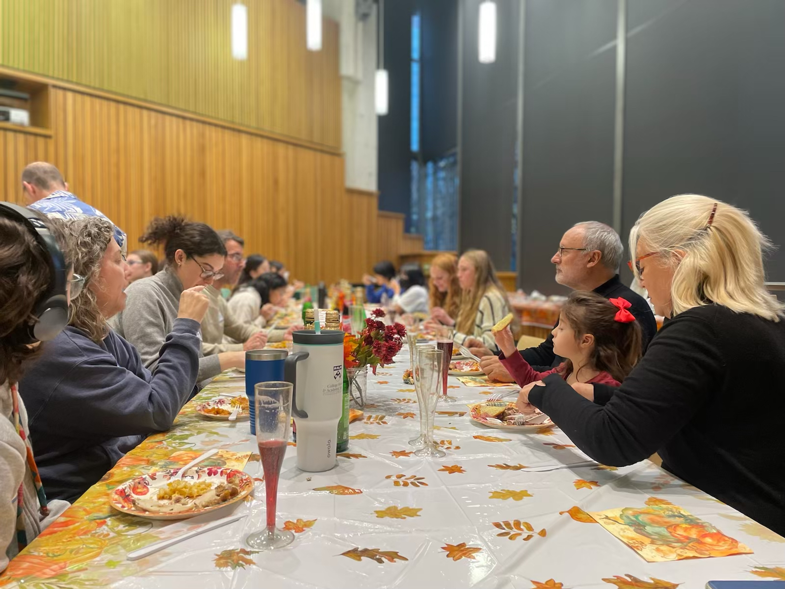 A group of people sit together at a long table with plates of food and Thanksgiving decor