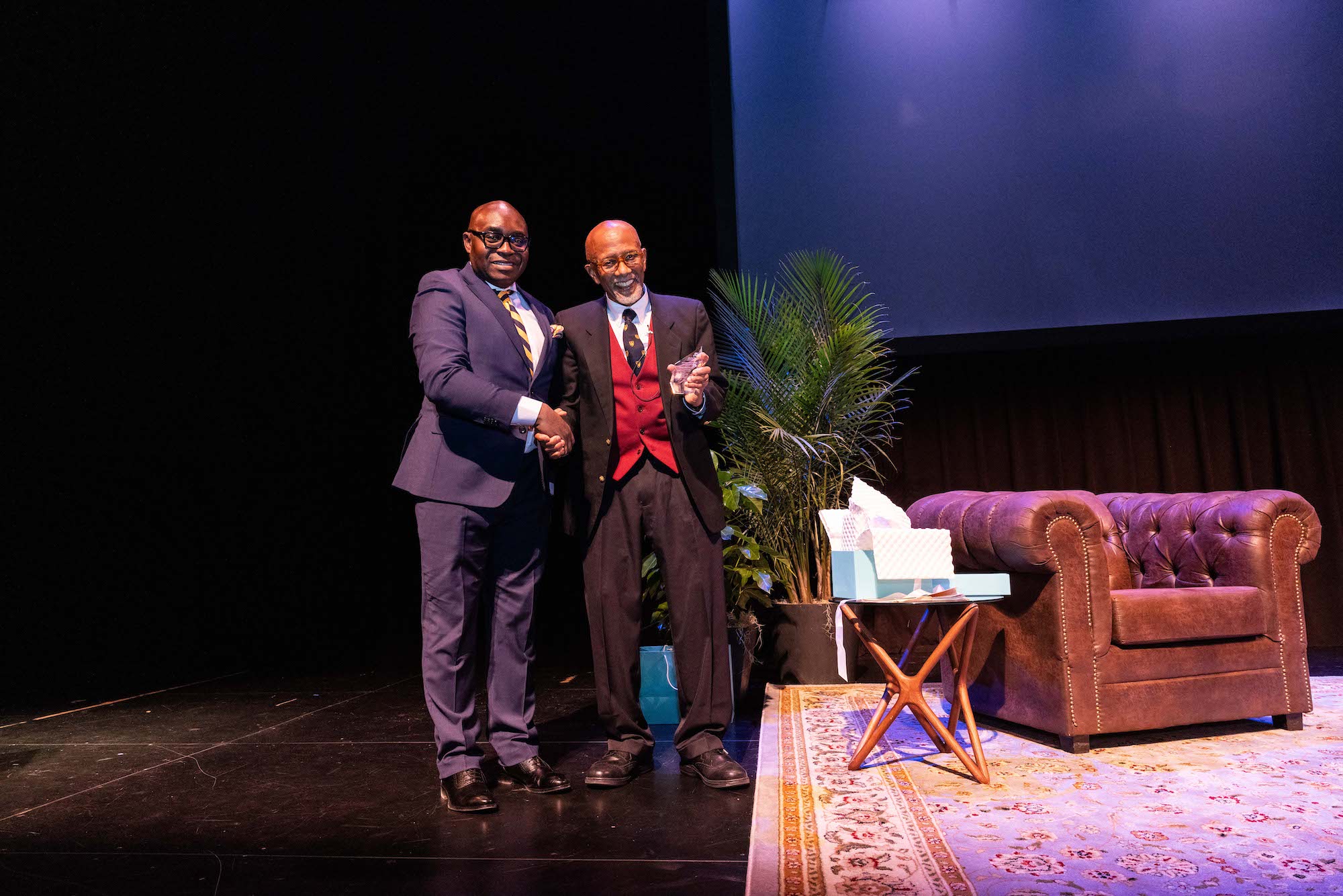 Wale Adebanwi and Orlando Patterson smile, shaking hands onstage