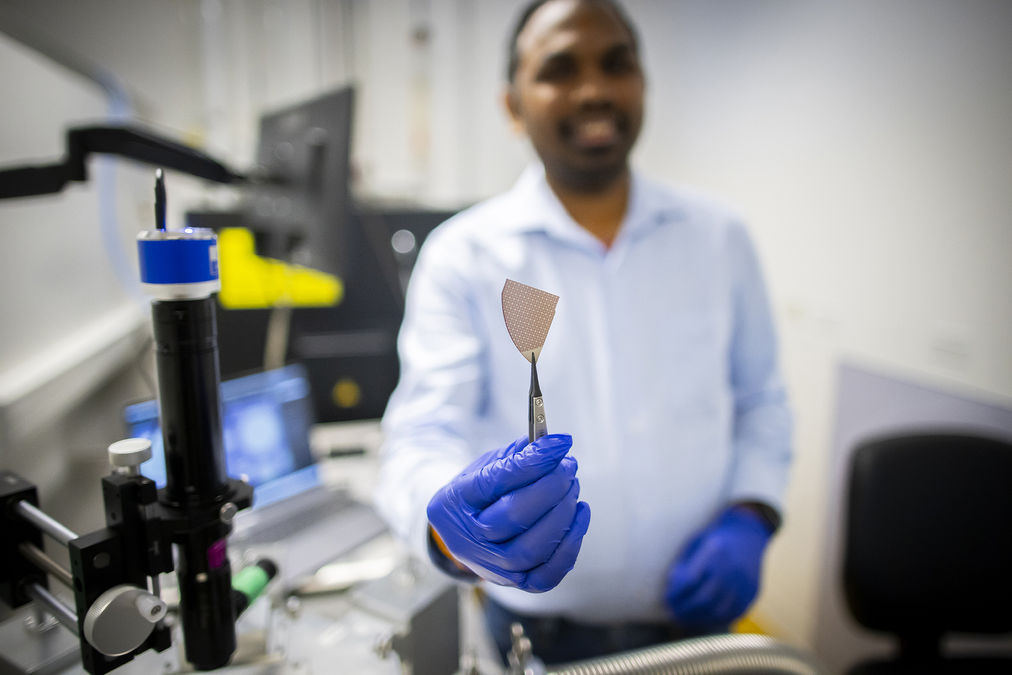 A researcher holds a specimen up with tweezers in a lab.