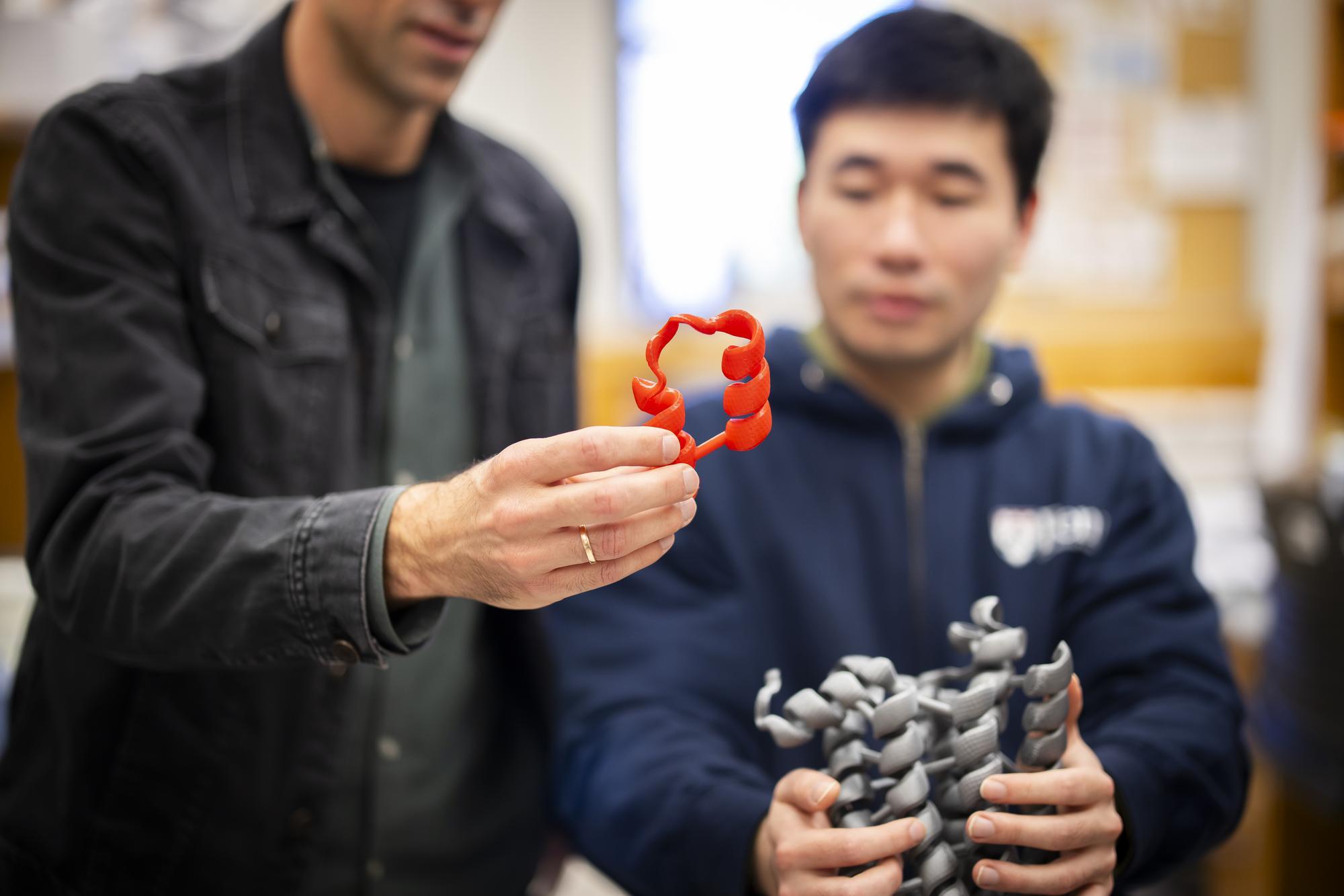 Two Penn researchers holding up pieces of a model.