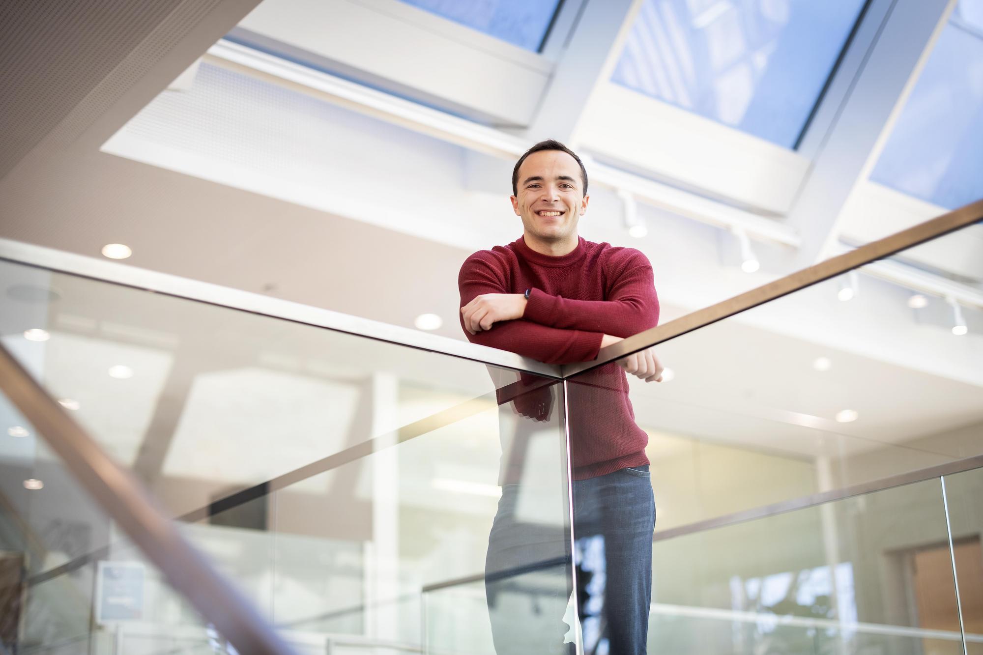 Alexander Schrier looks down from an upper floor of a building, standing behind waist-high glass panels.