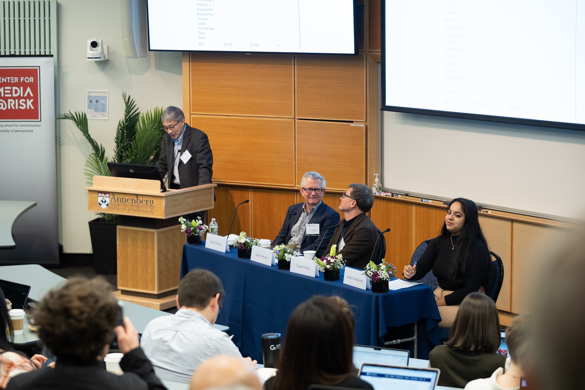 Guobin Yang talks at podium next to panel.