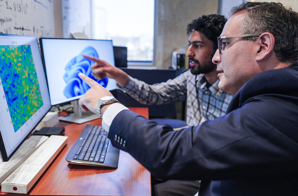 Iahn Cajigas and Qasim Qureshi review data on a desktop computer.