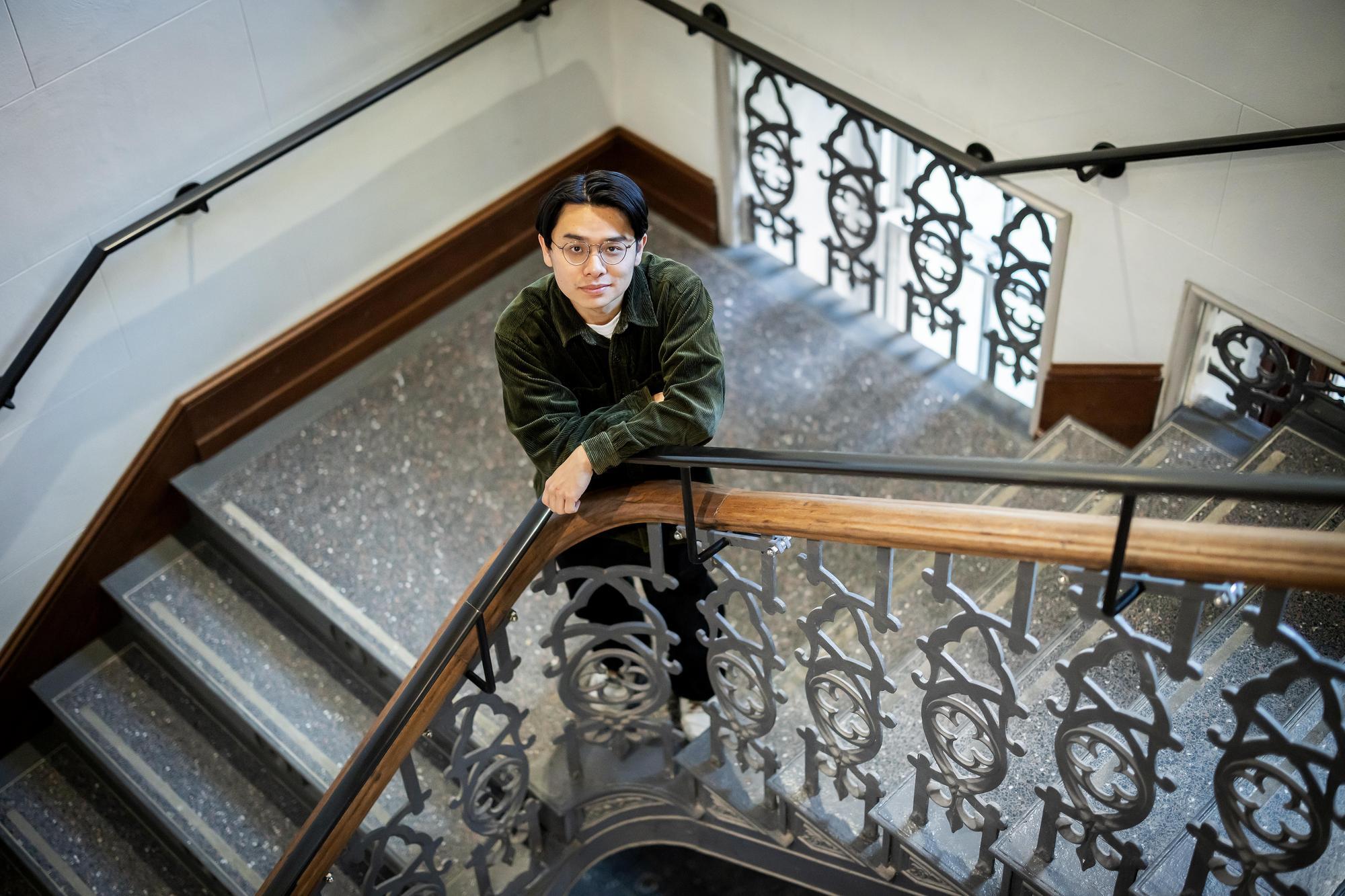 A man stands in a stairwell leaning on the banister.