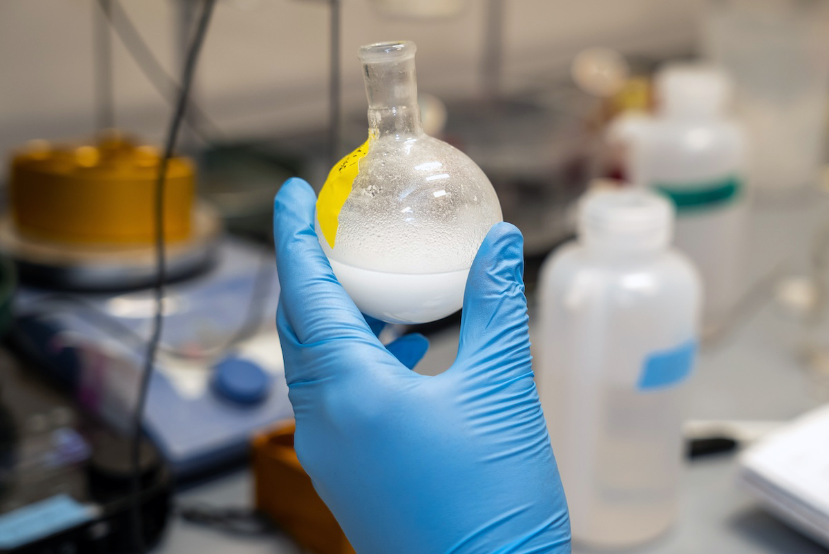 A gloved hand holding a beaker of lipids in a lab.