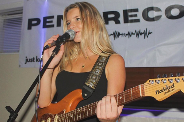 Grace Gramins sings into a microphone with a guitar.