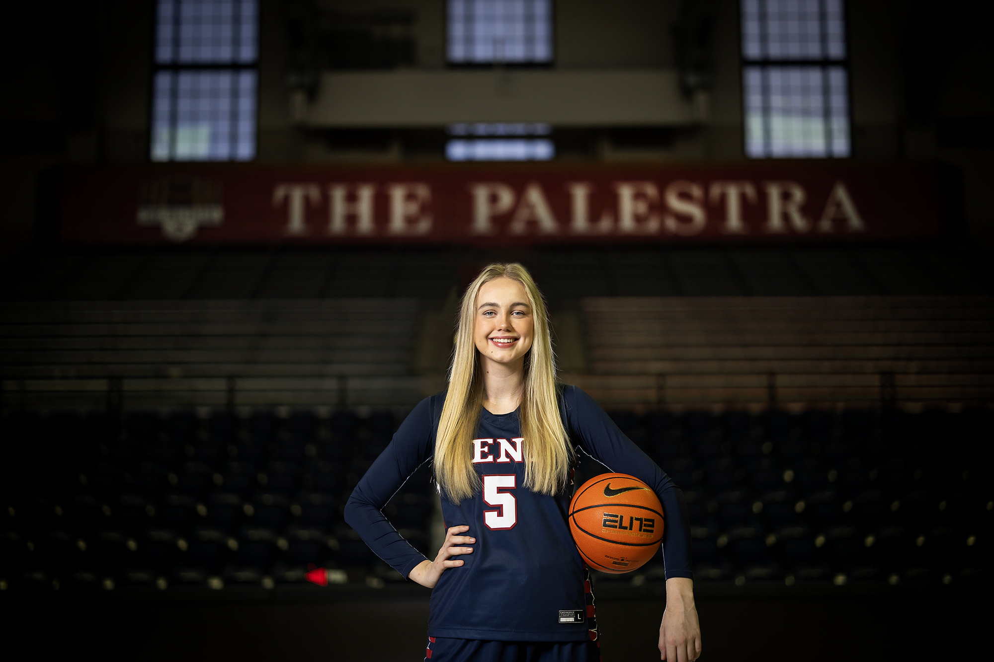 Stina Almqvist poses on the Palestra court in her uniform holding a basketball.