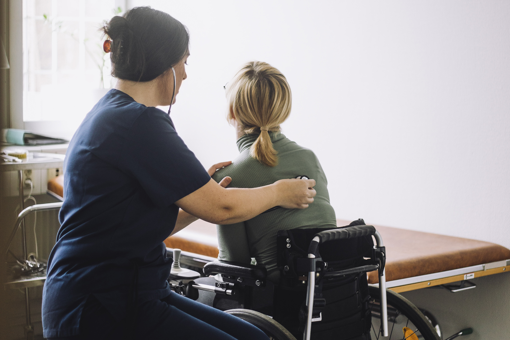 A nurse checks the heartbeat of a patient in a wheelchair.