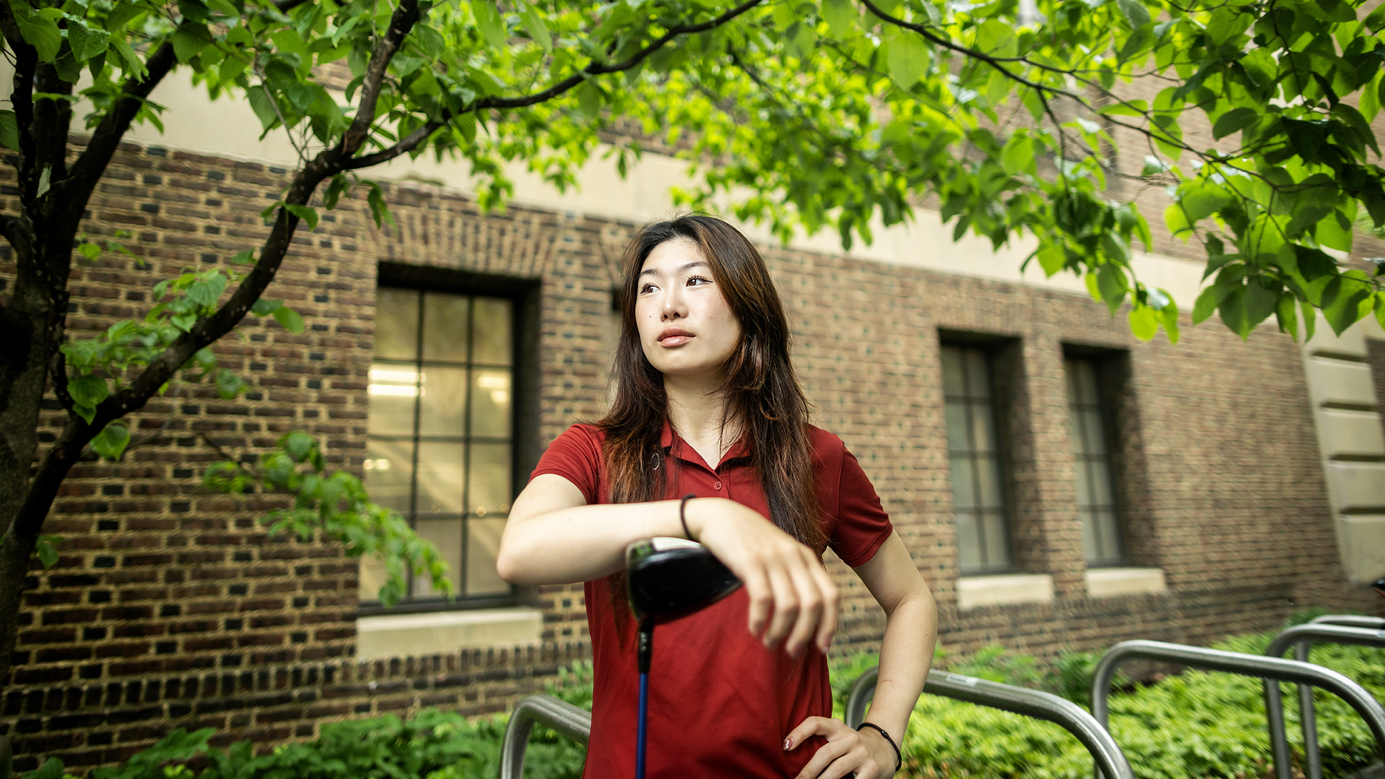 Julie Shin poses in front of the Palestra with her arm resting on her golf club.