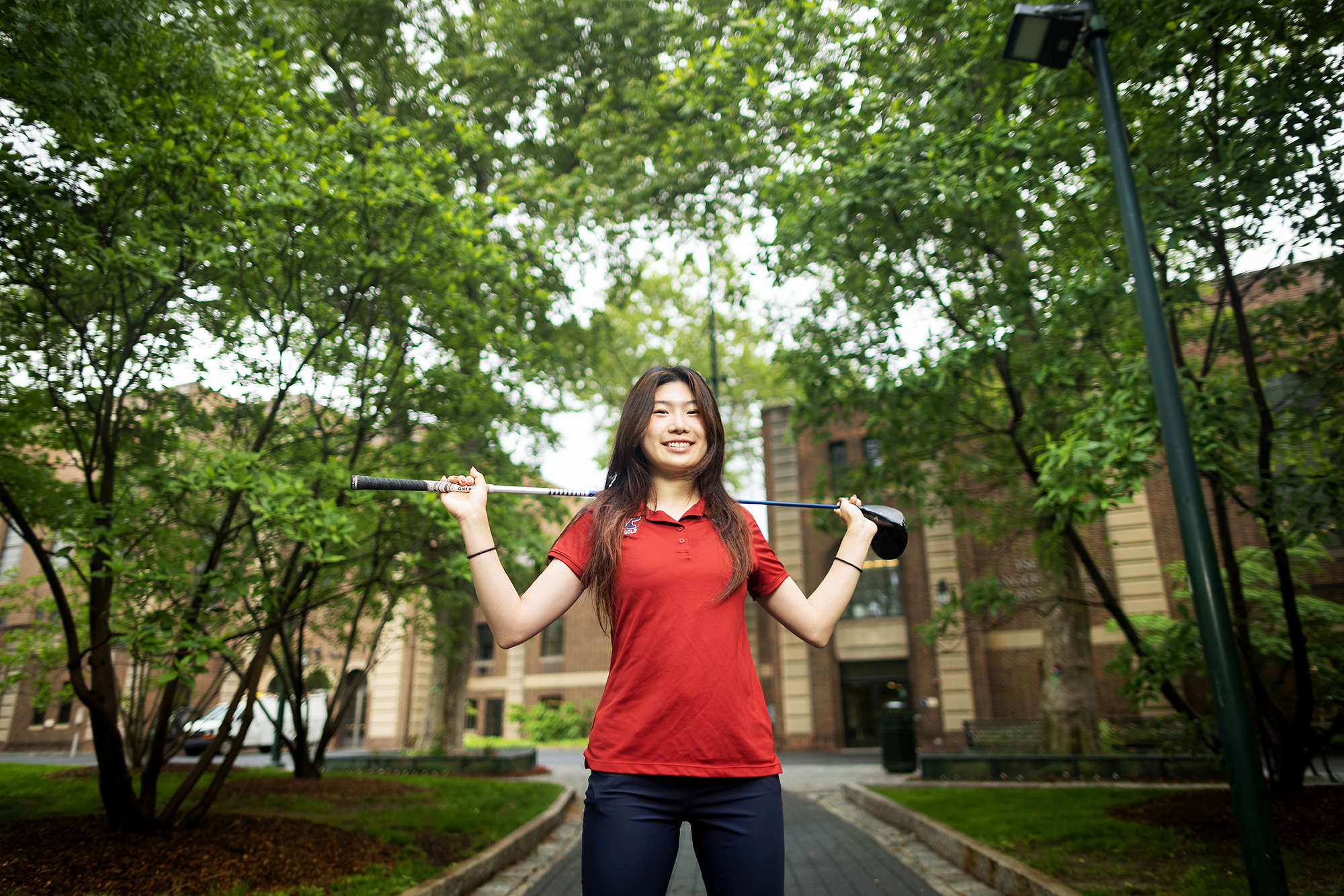 Julie Shin holds her gold club across her shoulders while standing in front of the Palestra.