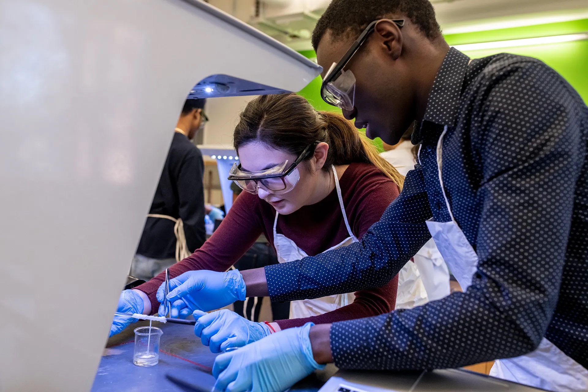 Two students wearing safety goggles performing research in a lab.