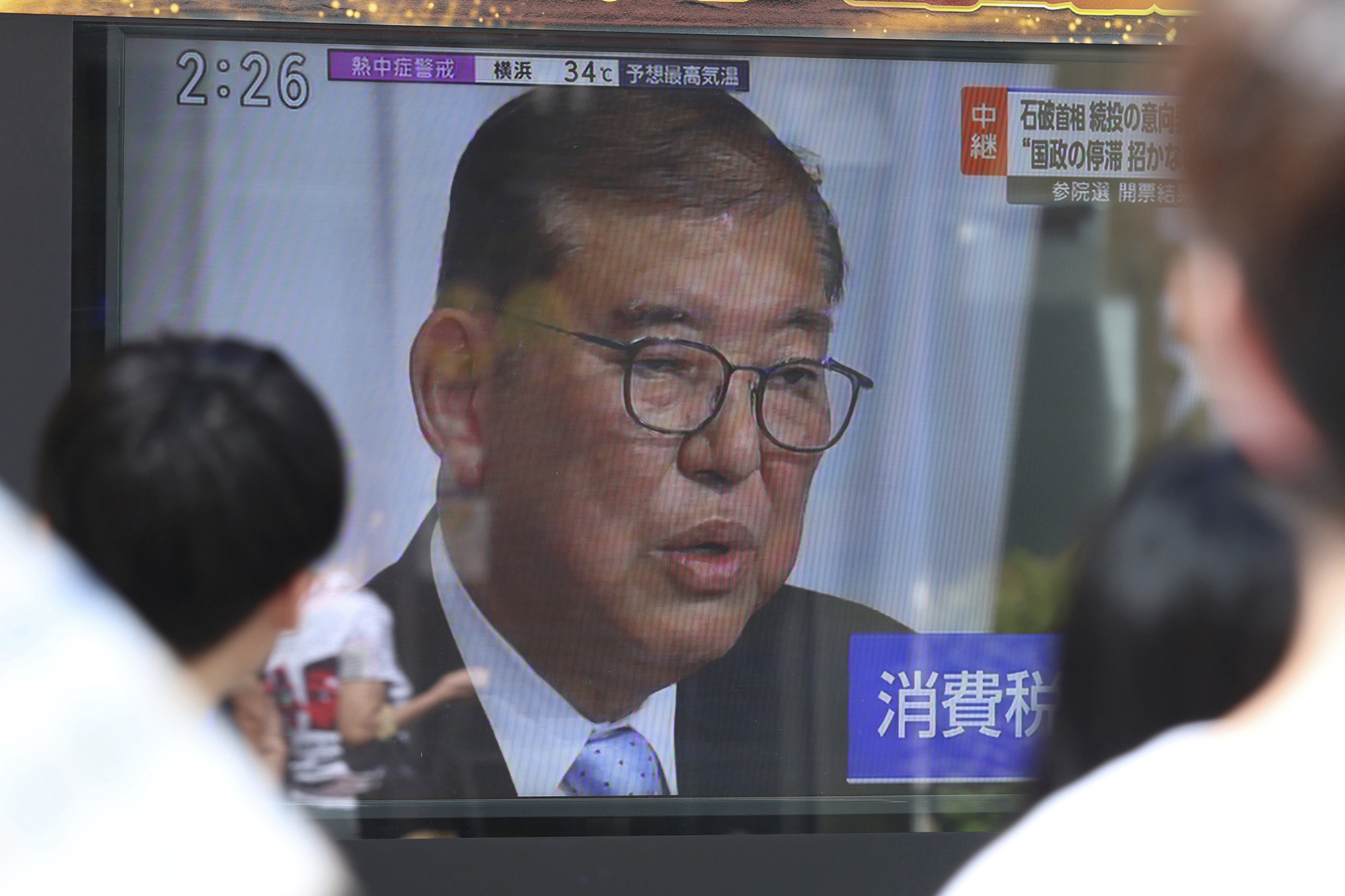 A man is seen on a television screen, framed by the heads of people watching.