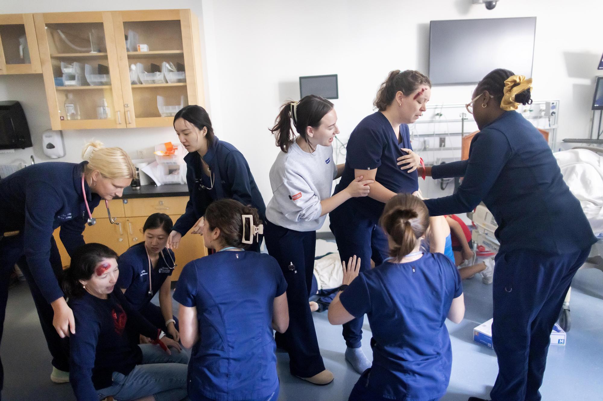 Nursing students help actors with fake blood in a simulation.
