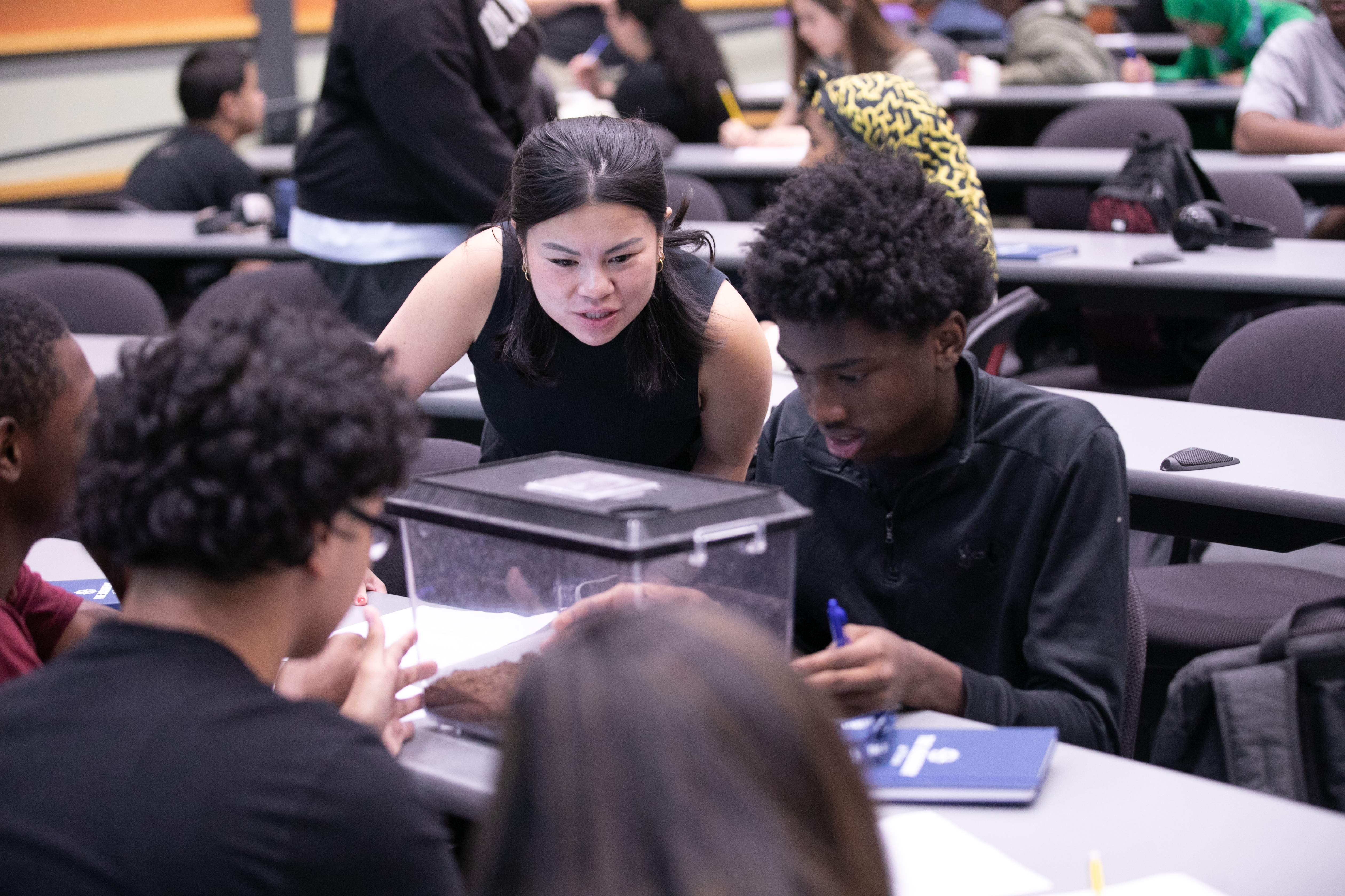 Instructor and student gaze at spider in a container.