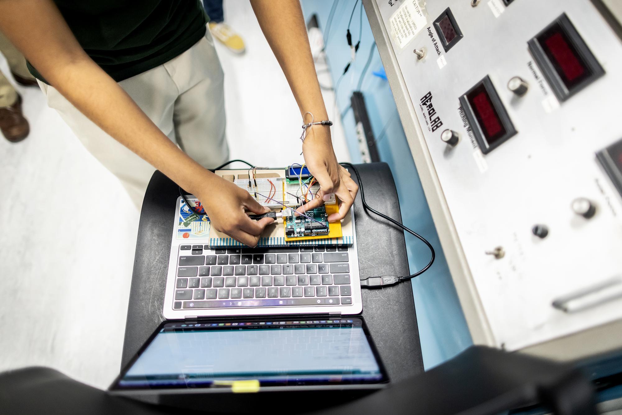 A student threads wires from a portable, modular computer into a laptop.