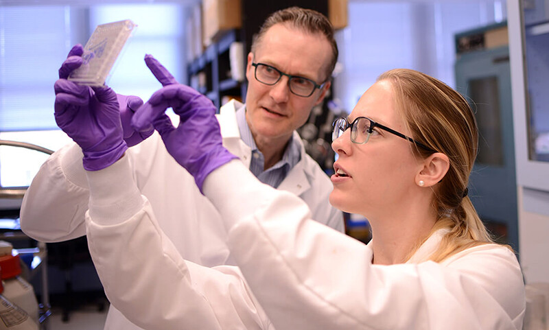 oliver-garden-and-sabina-hlavaty-wearing-latex-gloves-hold-up-a-plate-of-medical-cells-