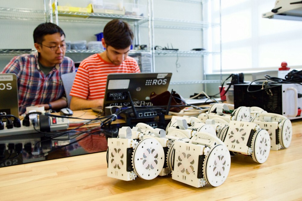 Two students work at a laptop behind cluster of SMORES modules 