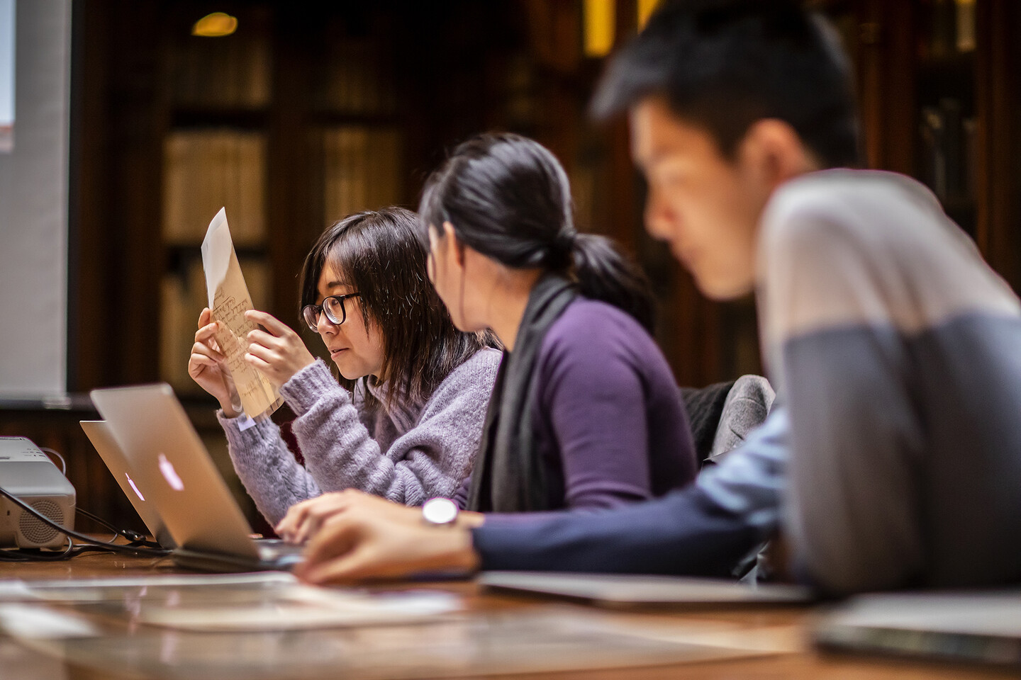 Student looking closely at a rare document while seated in a library.