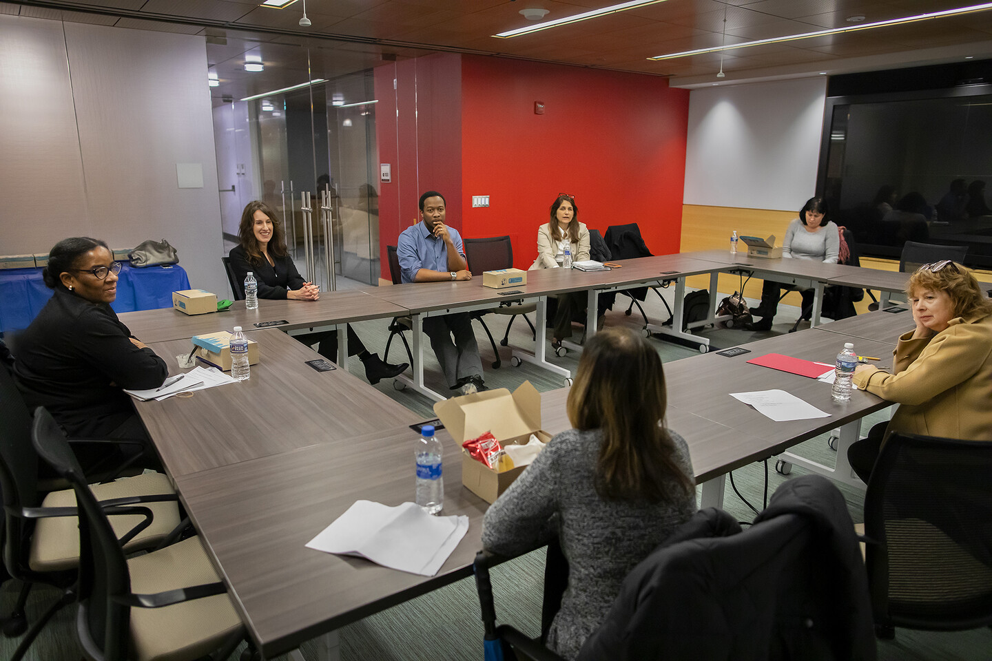 People sitting around a rectangular table in a room with a bright red wall. 