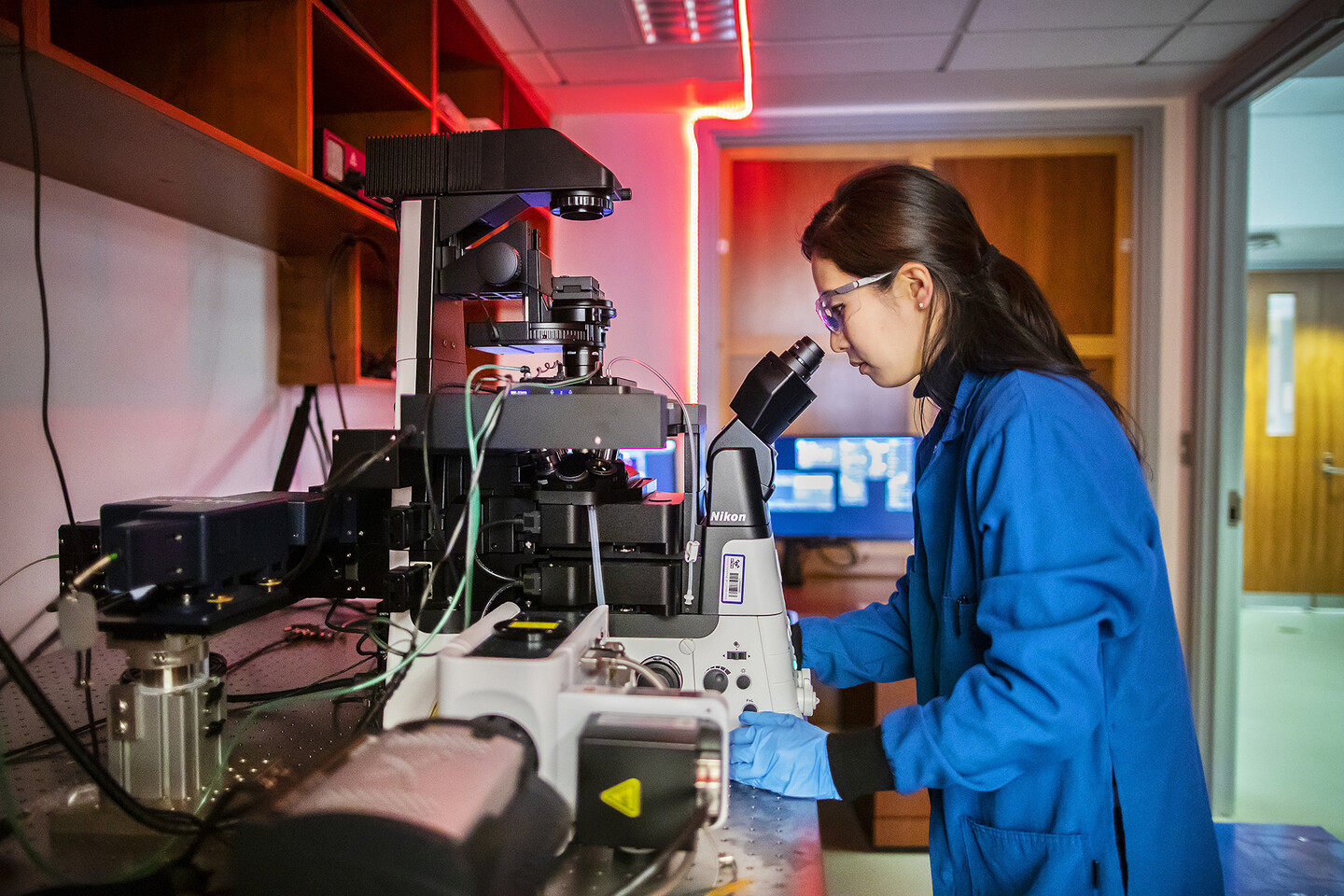 Jun looking into a microscope inside of a darkened laboratory