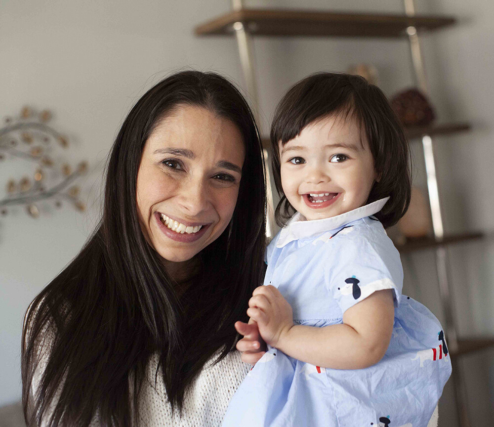 Erica holding her two-year-old daughter, both smiling at the camera.