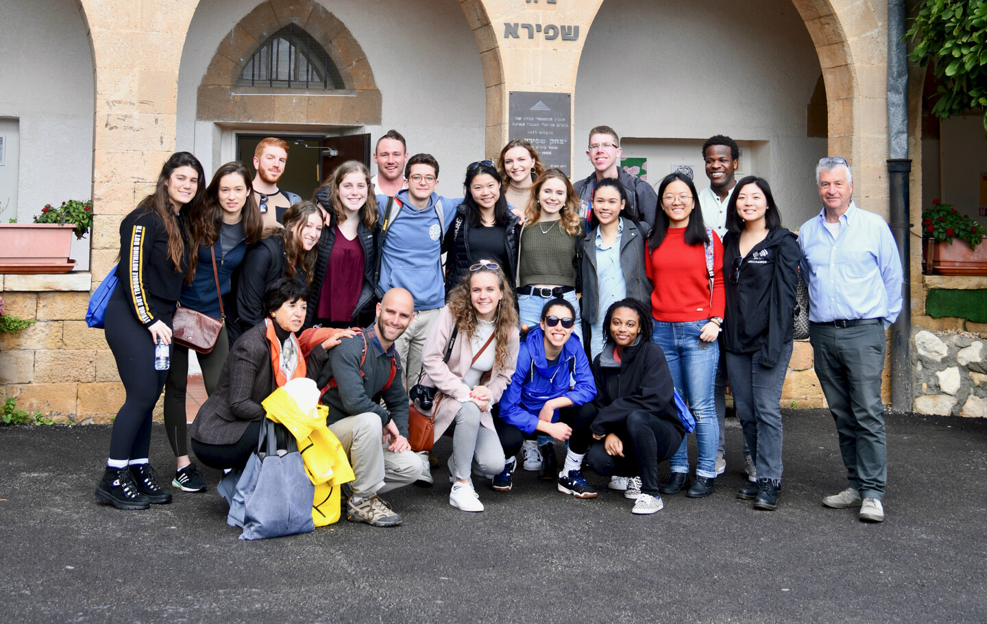 A group of college-age students standing in front of a building with Hebrew writing