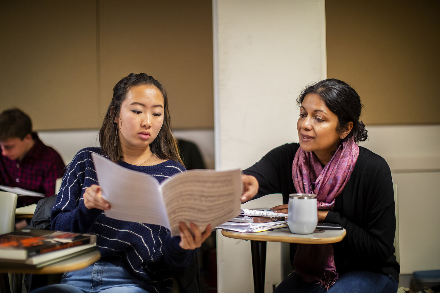 Professor gestures to music score held by student. 
