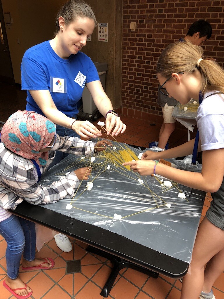 people building a triangle-shaped tower out of spaghetti and marshmallows