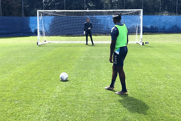 A person kicking a soccer ball into a net with a soccer goalie. 