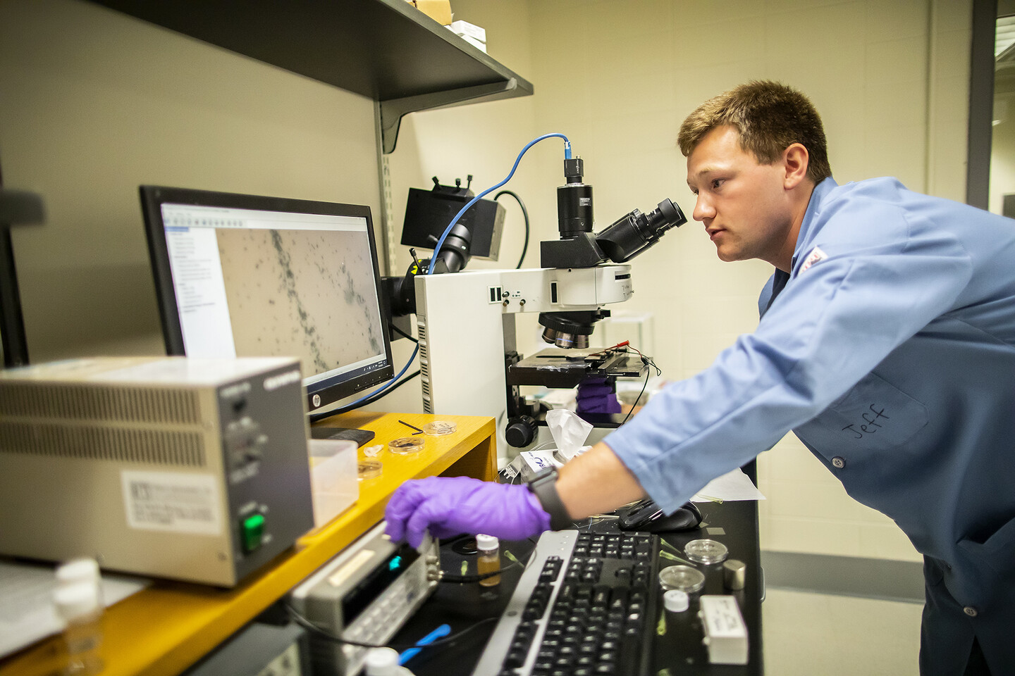 jeff mcneil looking at an image from a microscope on a computer while adjusting a dial