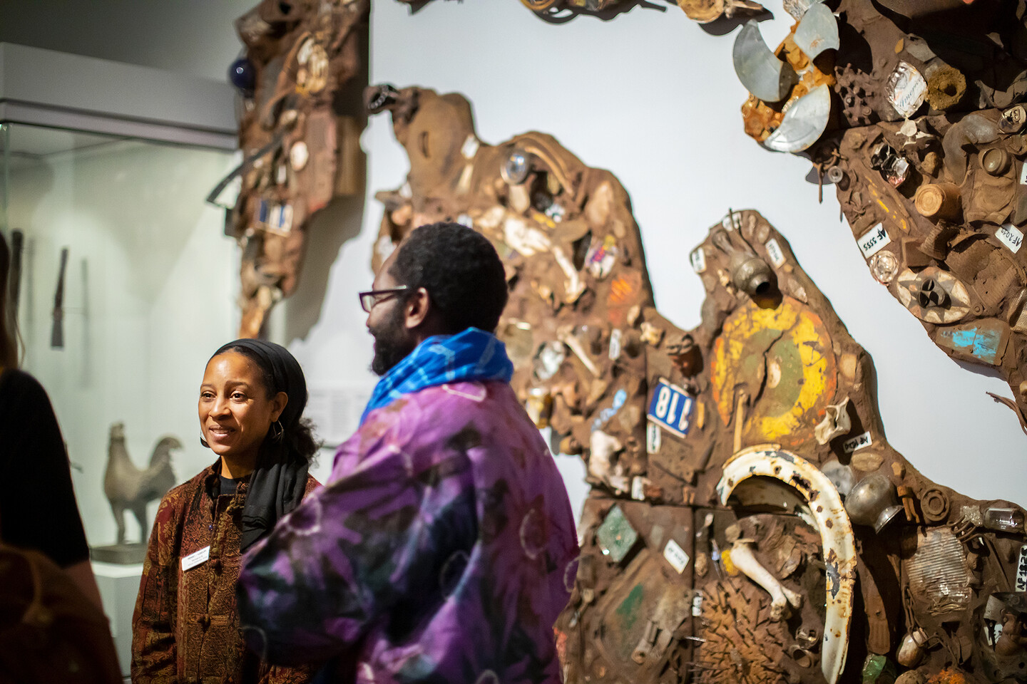 Two people stand in front of a mixed media assemblage