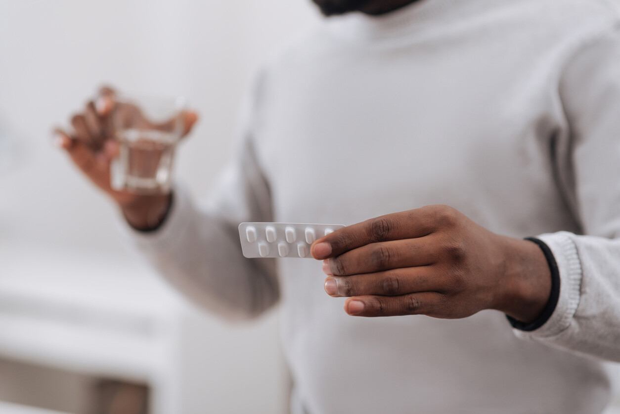 Person holding a packet of prescription pills and a glass of water